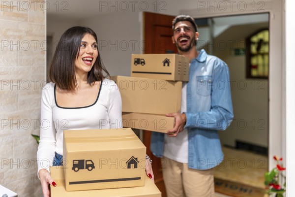 Cheerful homeowners carrying cardboard boxes, smiling as they enter their new apartment, embracing