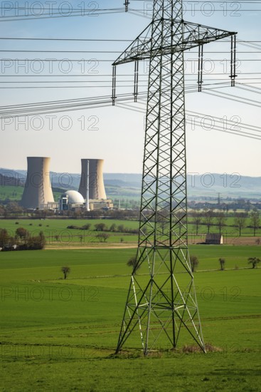 An electricity pylon stands in a green landscape with the Grohnde nuclear power plant in the