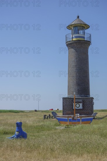 Brick lighthouse next to boat and blue sculpture in a meadow under blue sky, juist, north sea,