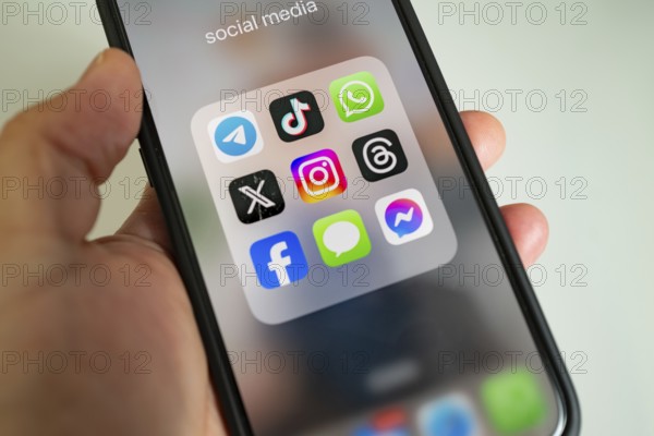 Close-up of a smartphone held in the hand, showing app icons, WhatsApp, Tik Tok, X, Facebook and