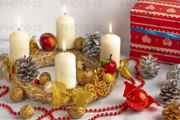 Advent wreath with four burning candles, red pearl necklace and Christmas decorations next to it