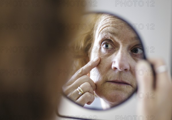 Symbolic photo on the subject of eye wrinkles. A woman looks at her eye wrinkles in the mirror.