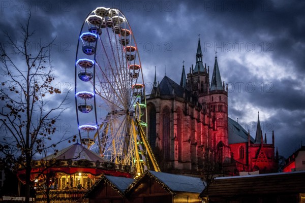 Ein beleuchtetes Riesenrad vor dem Hintergrund einer Kathedrale und einem dunklen Nachthimmel,