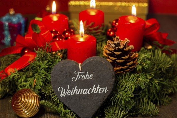 Heart with the inscription FROHE WEIHNAHCHTEN in front of an Advent wreath and Christmas