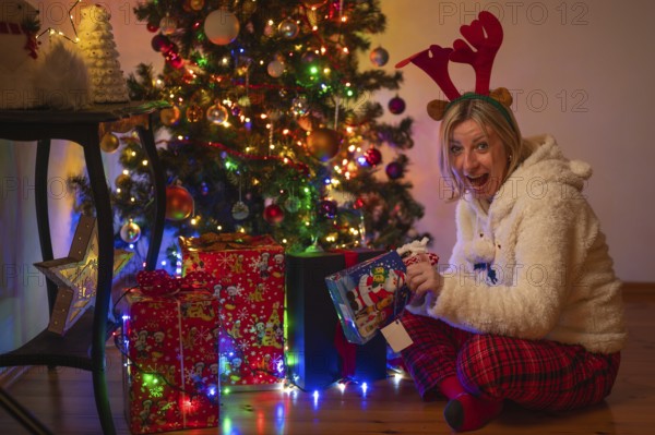 A woman in a Christmas costume opens a present under the Christmas tree
