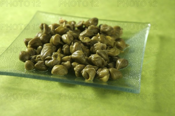 Capers with vinegar snack on a transparent plate, green background