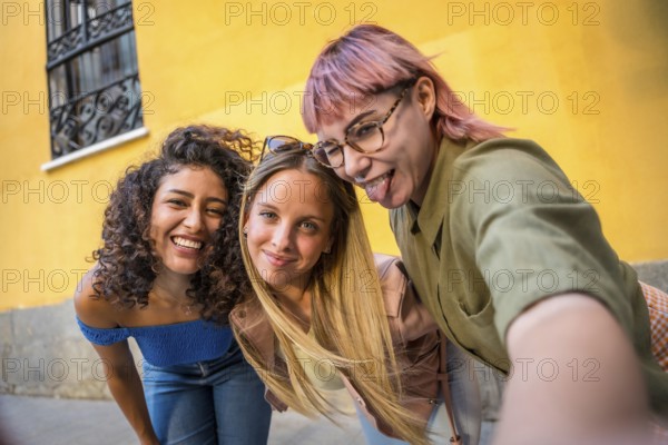 Happy female friends grimacing and sticking tongue out while taking selfie in the street