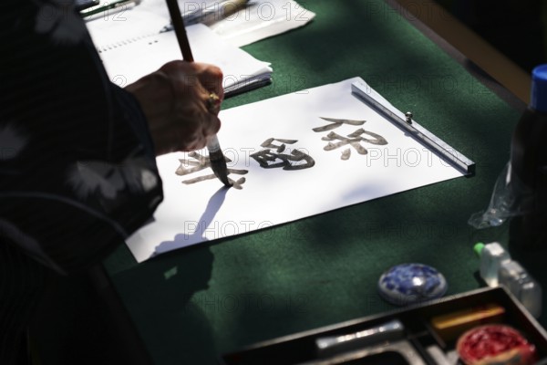japanese calligraphy, unrecognizable person writing kanji characters with ink brush on paper,