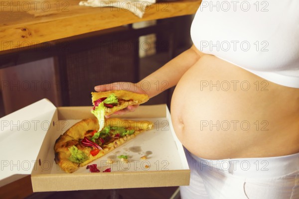 Young pregnant woman eating pizza at the kitchen. Pregnant nutrition