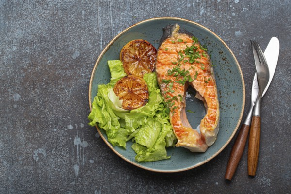 Grilled fish salmon steak and green salad with lemon on ceramic plate on rustic blue stone