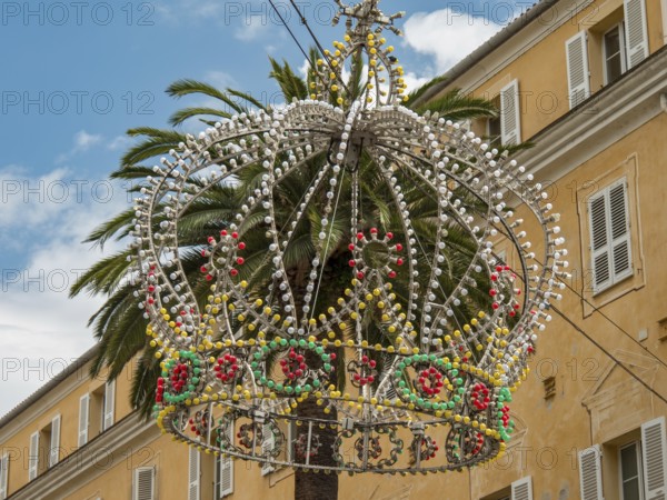 Colourful crown of pearls as decoration on a palm tree in front of a yellow building and blue sky,