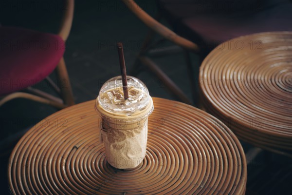 Iced coffee cup on a round rattan table surrounded by wicker chairs, evoking a cozy vibe