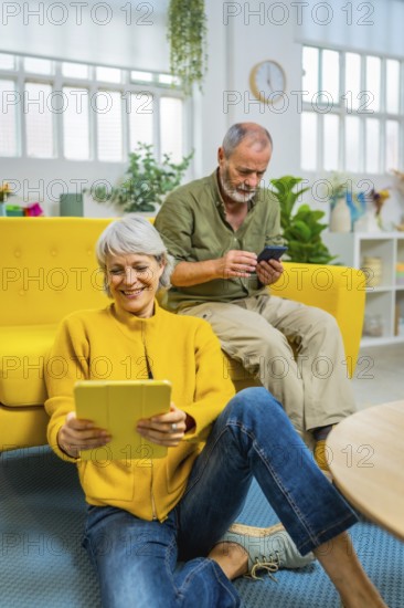 Senior couple using digital tablet and mobile phone spending time relaxed at home
