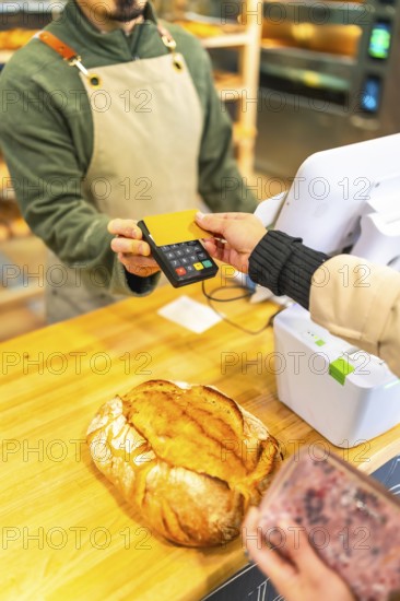 Vertical cropped photo of the hands of a woman paying using credit card in a modern bakery