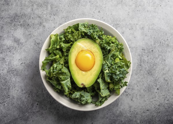 Salad bowl with kale for balanced menu, raw egg yolk in fresh cut half avocado rich in healthy fats