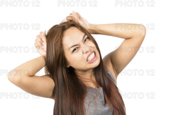 A frustrated Asian girl in gray with light brown hair, clenching her teeth, pulling her hair during