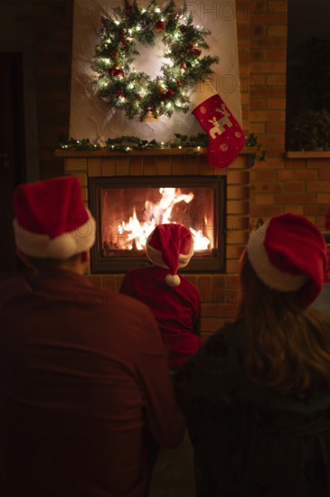 Family wearing Santa Claus hats sitting in front of the fireplace. Poland