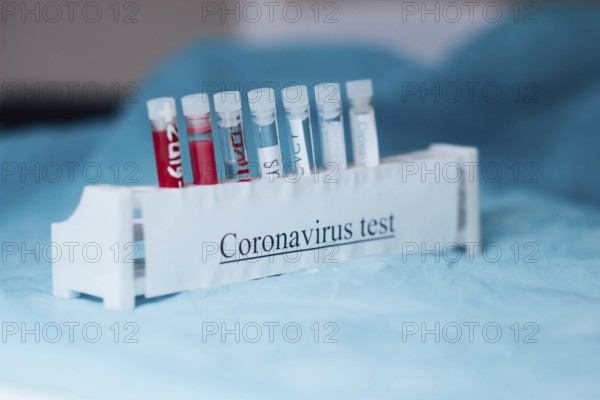 Test tubes labeled for coronavirus testing placed in a holder on a blue surface