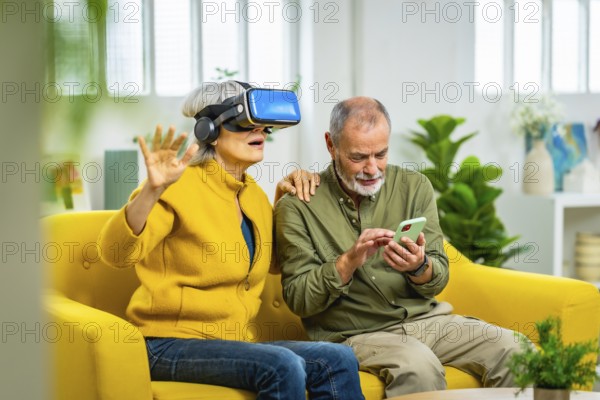 Senior woman using virtual reality glasses next to her husband sitting on the sofa using mobile app