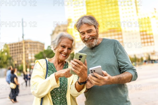 Frontal portrait of a cute modern senior couple having fun using smartphone in the city
