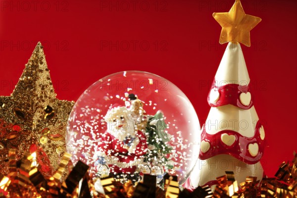 Santa claus figurine on a glass snowing ball, red background studio shot