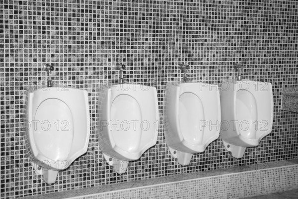 Bathroom urinal in a row with gray tiles black and white