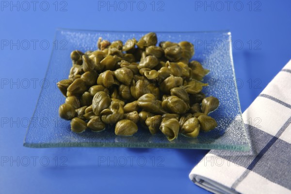 Capers with vinegar snack on a transparent plate, blue background