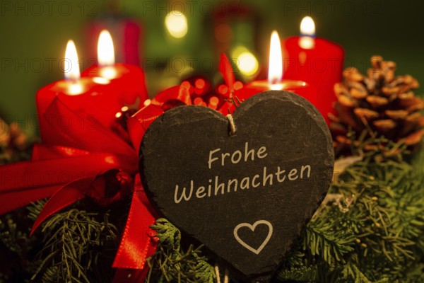 Christmas greetings: Heart with the inscription FROHE WEIHNACHTEN in front of Christmas decorations