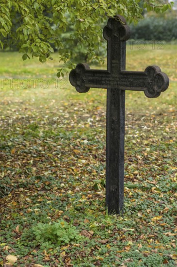 Weathered iron cross marking a grave in a cemetery during the fall season