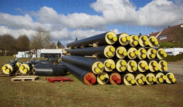 Stacked district heating pipes and district heating lines with yellow ends lie piled up in a meadow