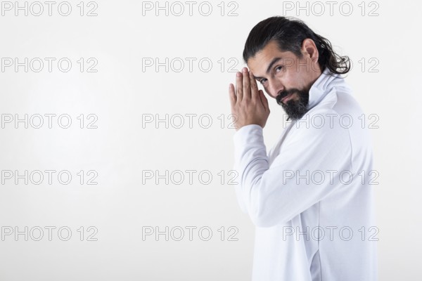 A man dressed in white clasping hands while looking at camera over white background. Tadasana yoga