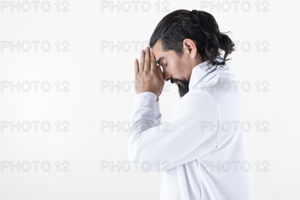 A man dressed in white clasping hands while meditating over white background. Tadasana yoga pose.