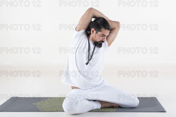 A man dressed in white doing yoga on a mat over white background. bharadvajasana yoga pose. Studio