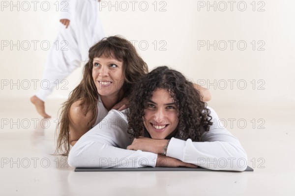 Portrait of a young man dressed in white yoga clothes lying on a mat while looking at camera with a