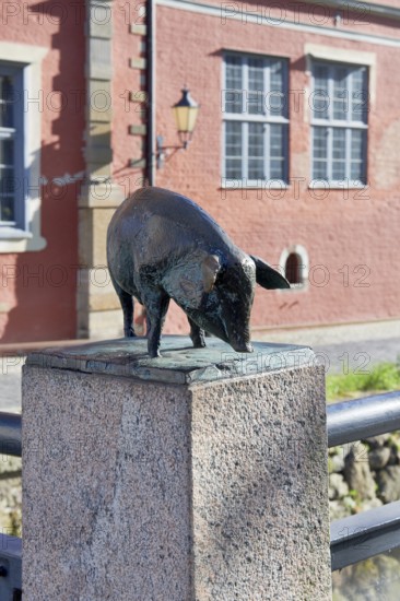Bronze sculpture of a wild boar on a pedestal in front of a red building, pig bridge with a group