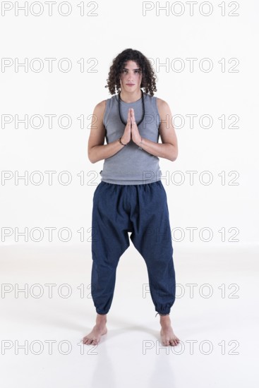 Young man clasping hands while looking at camera over white background. Meditation concept. Studio