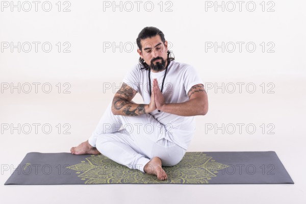 A man dressed in white doing yoga on a mat over white background. Front view