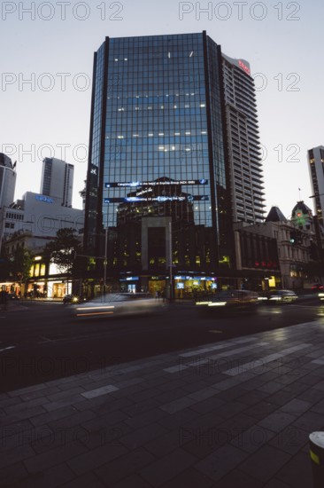 High-rise building with reflective glass façade at dusk, city lights and passing cars, new Zealand