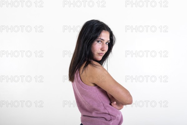 Beautiful young woman looking at camera with her arms folded, wearing a pink t-shirt. Studio shot.