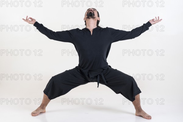 A man dressed in black doing yoga over white background. Utkata konasana yoga pose. Studio shot