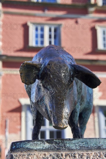 Bronze sculpture of a wild boar in front of a red building with windows, pig bridge with a group of