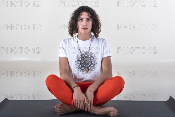 Man sitting cross-legged on a mat about to meditate while looking at camera over white background.