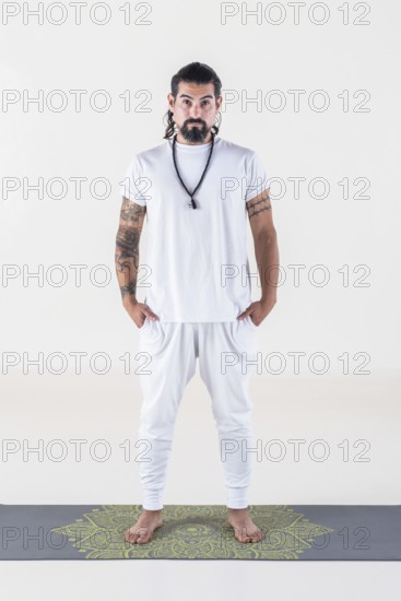 Portrait of a man dressed in white yoga clothes over white background while looking at camera.