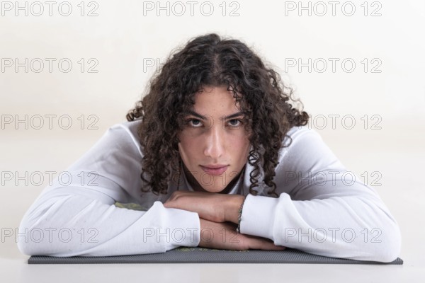 Portrait of a young man dressed in white yoga clothes lying on a mat while looking at camera over