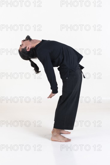 A man dressed in black doing yoga over white background. Suryanamaskar yoga pose. Studio shot
