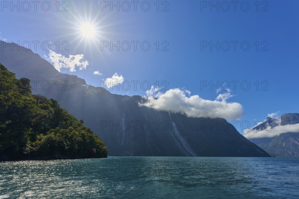 Clear sun over a fjord, surrounded by majestic mountains and a slightly cloudy sky, summer, Milford
