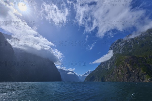 Sunlit mountains surrounded by deep water and clouds, summer, Milford Sound, Te Anau, Fiordland
