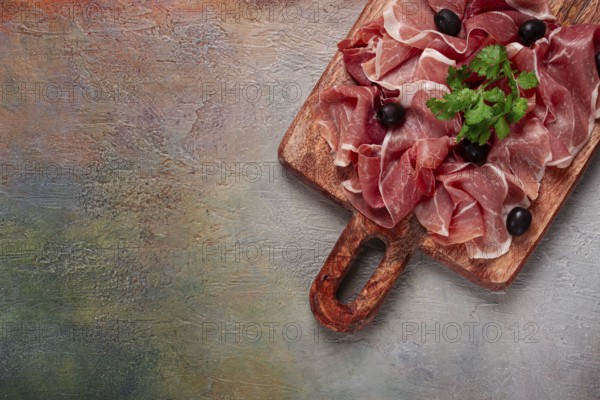 Sliced prosciutto, on a cutting board, with olives and herbs, snack, breakfast, no people