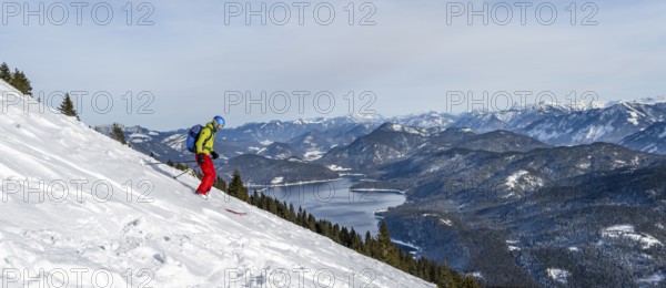 Skiers skiing down the Simetsberg, view of Walchensee and mountain panorama, Estergebirge, Bavarian