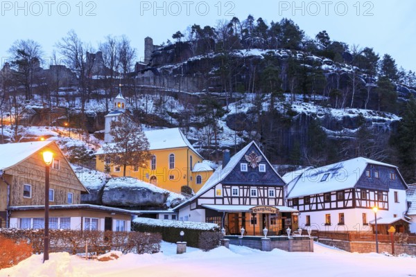 Striking half-timbered houses and mountain church in front of Mount Oybin with ruins, snow and